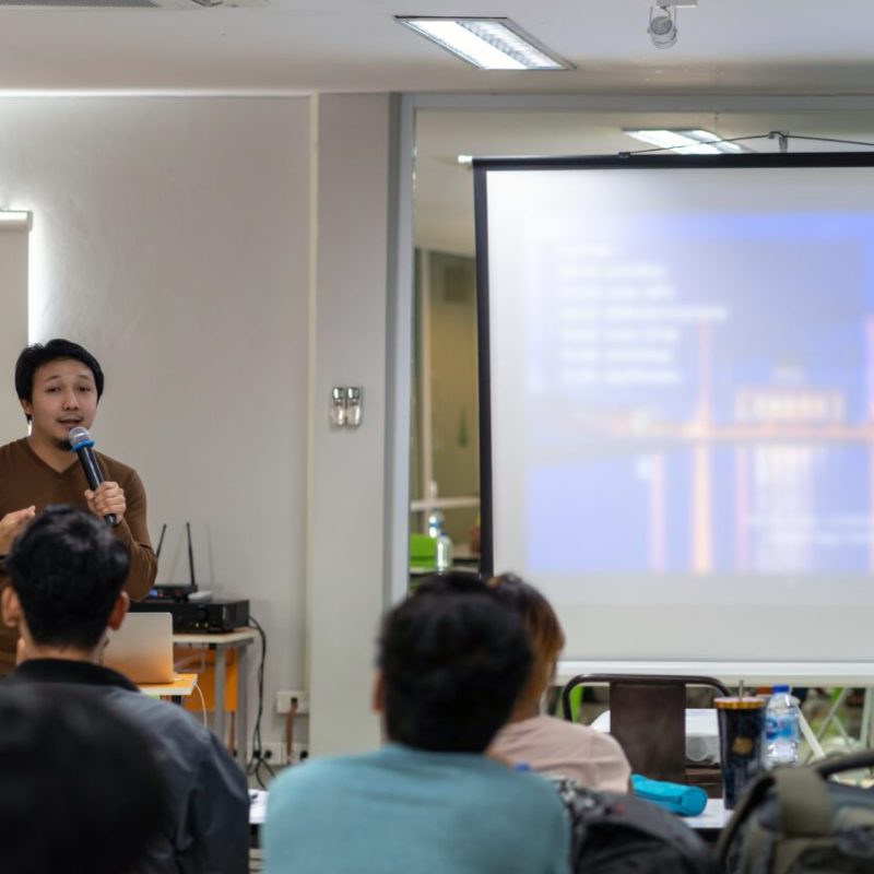 asian-speaker-or-lecture-with-casual-suit-on-the-stage-in-front-of-the-room-presenting-e1700115849214.jpg