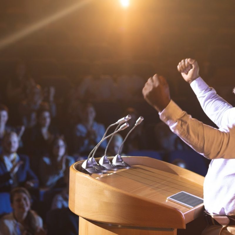 businessman-standing-near-podium-and-giving-speech-to-the-audience-in-the-auditorium.jpg